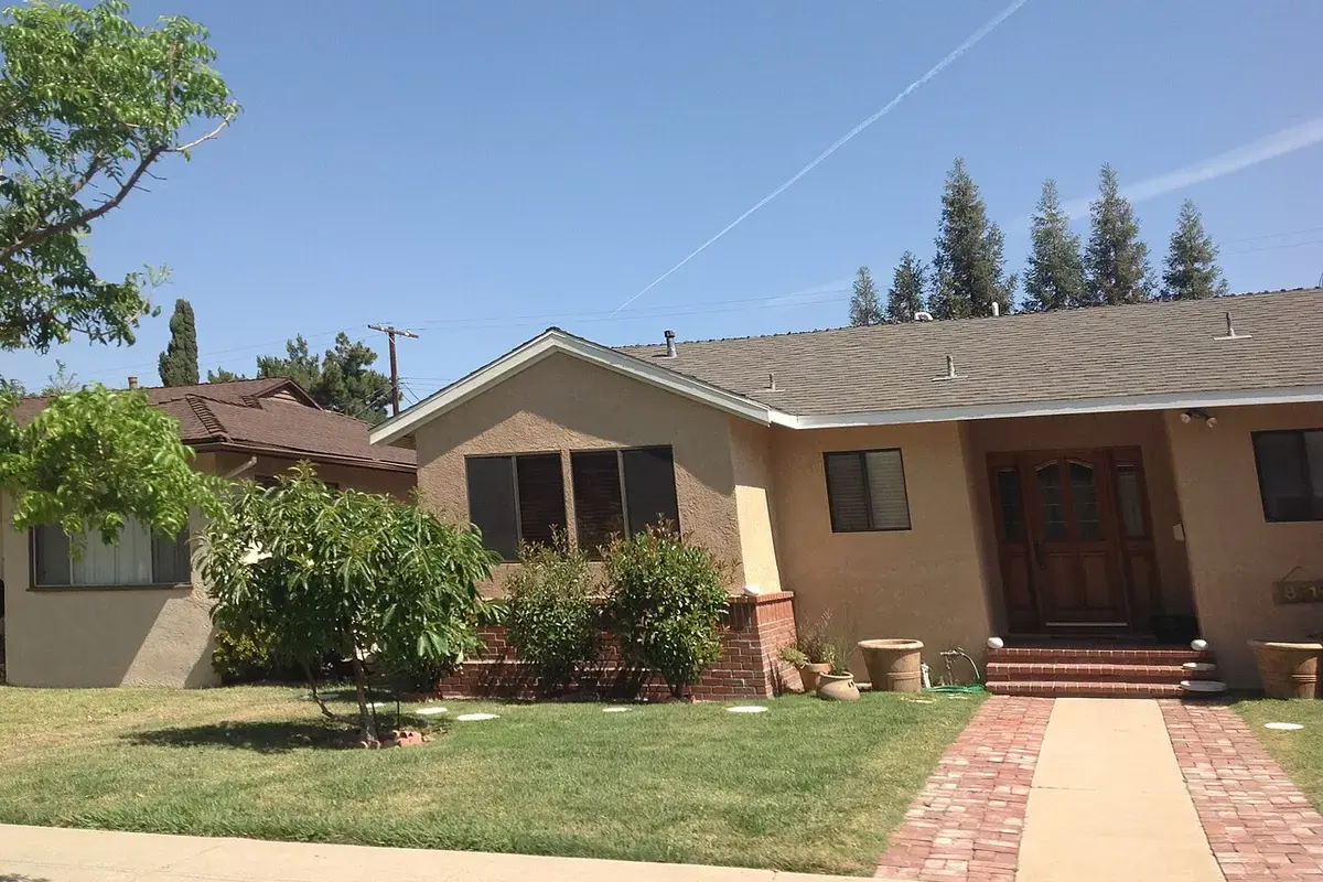 A single-storey postwar stucco house with a front lawn on a residential street in Reseda, Los Angeles.