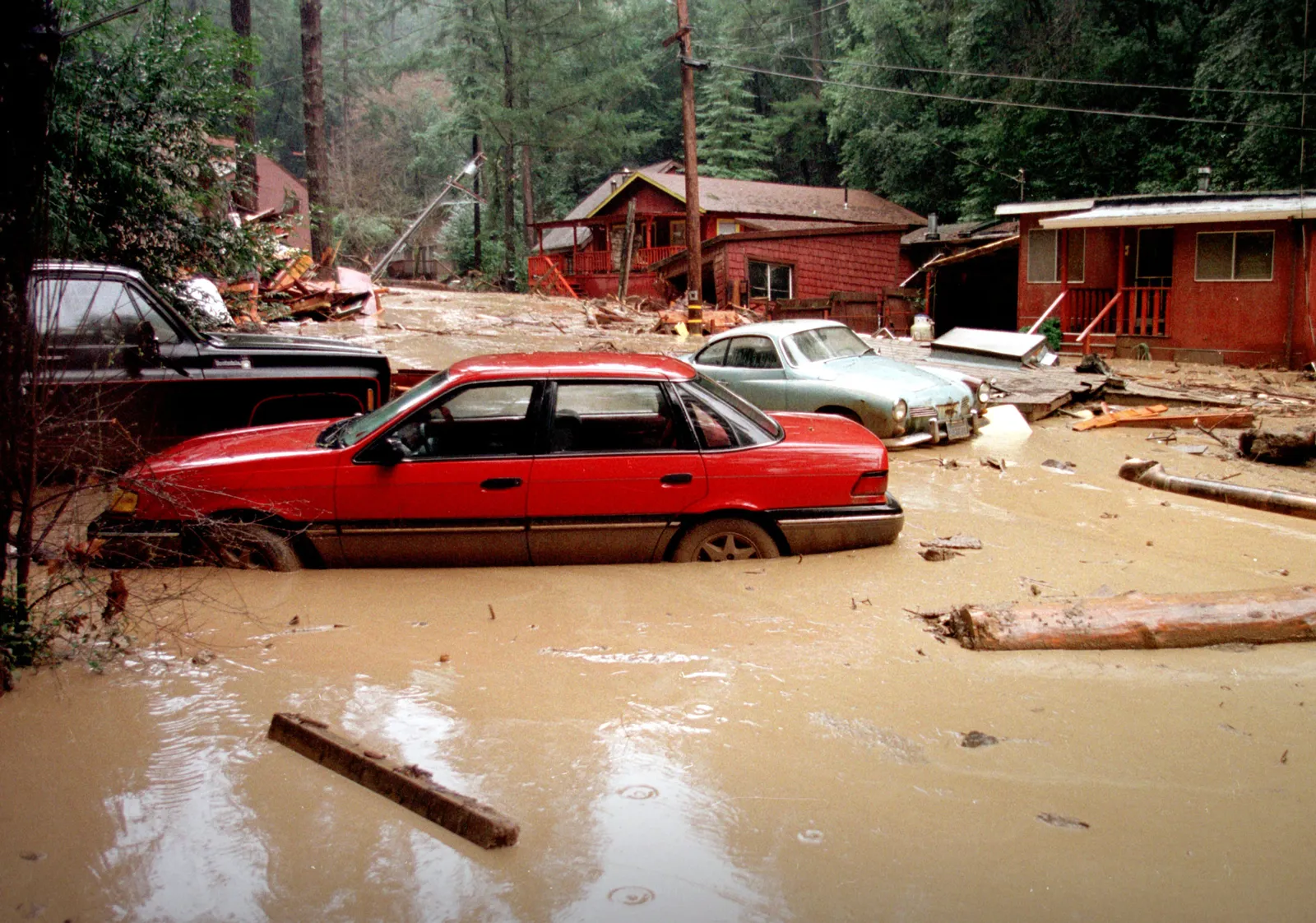 Cars sunk to their doors in mud and debris on a street of red wooden cabins in Rio Nido, Sonoma County, after a mudslide during the 1997-98 El Niño storms.